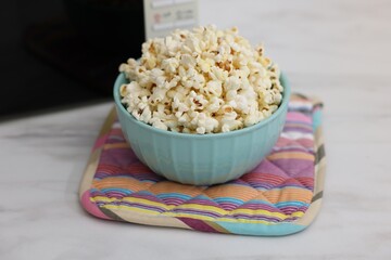 Tasty popcorn in bowl near microwave oven on light marble table, closeup