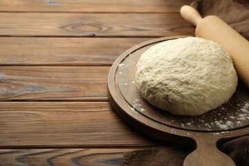 Fresh dough and rolling pin on wooden table, closeup. Space for text