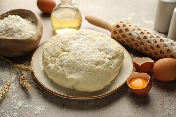 Fresh dough, ingredients and rolling pin on grey table, closeup
