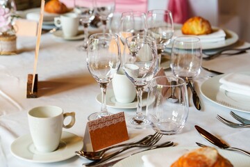A beautifully set table featuring wine glasses and a name tag. The white tablecloth is adorned with pink napkins, complemented by pink and white flower decorations.