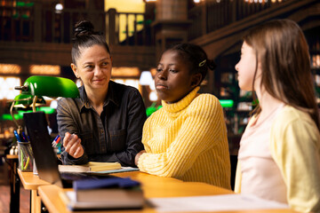 Preteen scholars collaborating with their tutor in a learning environment, working on school projects and developing critical classroom skills. Woman mentoring her students in the library.