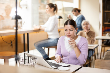 Young woman spending time in cozy coffeehouse with laptop and coffee