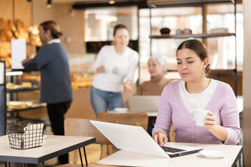 Calm woman sitting in cafe diligently doing her work on laptop