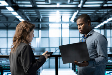 Computer scientists in data center using laptop and tablet, executing security patches, verifying...