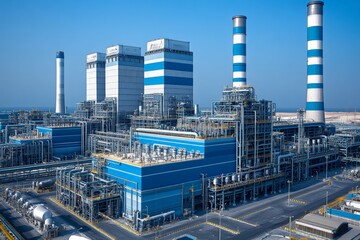 Industrial power plant with smoke stacks and blue structures under clear sky during daytime operation