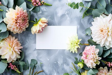 Gray background with eucalyptus branches and pink and white dahlia flowers surrounding a blank card