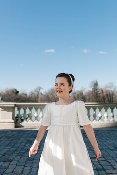 Girl in elegant First Communion dress under clear blue sky