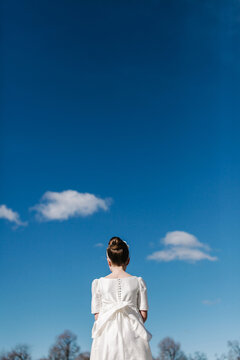 Girl in white First Communion dress under clear blue sky