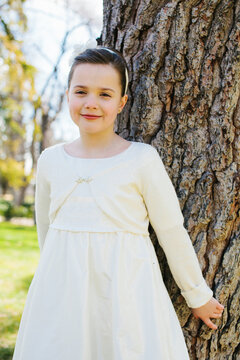 Young Girl in First Communion Dress by Tree in Sunlit Park