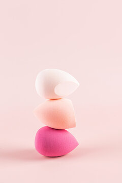 Balanced stack of three colorful makeup sponges on pink background