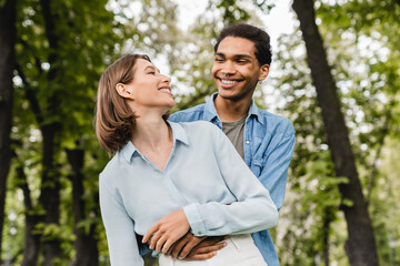 Fototapeta premium First true feelings. Young happy mixed-race couple students hugging embracing together in city park walking on romantic date. Love and relationship concept. Love at first sight.