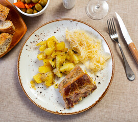 Traditional Central European meal featuring baked pork, seasoned potatoes, and tangy sauerkraut, served with bread and olives for hearty lunch