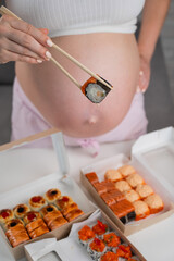 A pregnant woman stands at a table with rolls. Close-up of the belly.