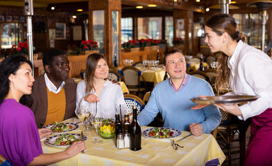 Two multiracial couples talking and with waitress and making orders in restaurant.