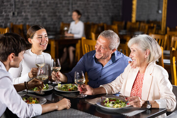 Elderly couple and young couple chatting and enjoying dinner in restaurant