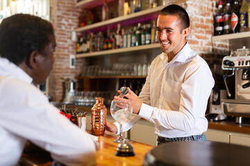Bartender shaking cocktail for friends, they drinking in nightclub