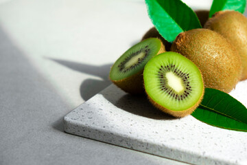 Ripe kiwi fruits in sunlight. Heap of whole kiwi fruits with green leaves and fresh cut kiwi on...