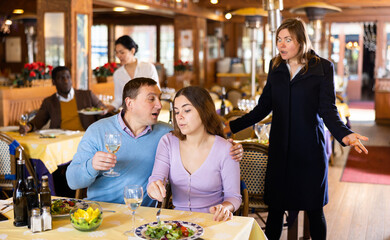 Resentful wife scolding her husband spending time with another woman at dinner in restaurant