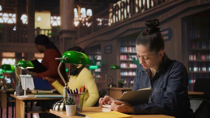 Woman tutor reading a book and doing a brief to complete her notes, creating accurate learning materials for her private lessons and mentoring in an academic environment. Camera A.