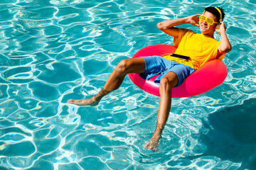 Young teenage boy relaxing on pool float with headphones on