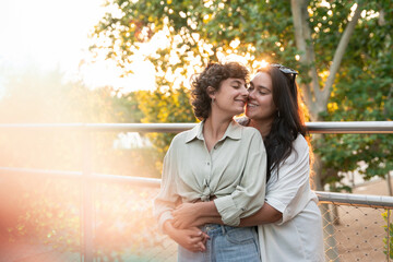Lesbian couple embracing in sunlight at park railing