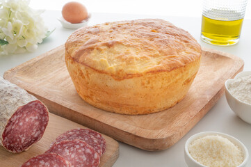 Traditional Easter pizza cake from central italy, with pamigiano cheese and pecorino romano cheese, accompanied by salami and eggs , horizontal close up photo with white wooden table 