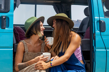 A lesbian couple enjoying coffee by a van on a sunny day