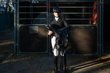 Equestrian holding a saddle by a stable in dressage attire
