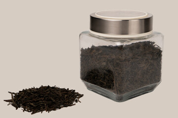 A close-up of loose black tea leaves arranged neatly on a white backdrop, accompanied by a glass...