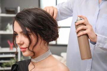 Professional hairdresser applying hair spray on young woman's hair in beauty salon