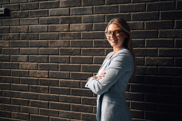 Smiling businesswoman standing with folded arms in front of brick wall