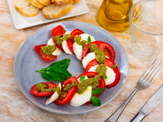 Fresh caprese salad with mozzarella, tomatoes, basil and pesto sauce on plate
