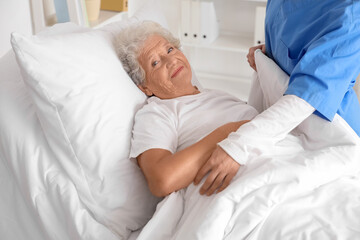 Obraz premium Female nurse putting senior woman to bed in bedroom