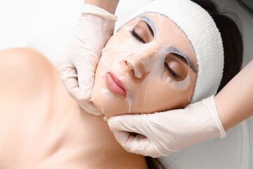 Young woman with facial sheet mask relaxing in spa salon