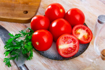 Fresh red tomatoes on wooden table with kitchen knife and bunch of parsley.