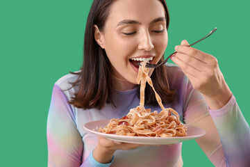 Young woman eating tasty pasta on green background, closeup