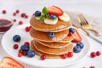 Plate with tasty pancakes, cutlery and berries on white table