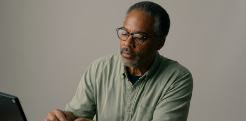 Fototapeta premium Man wearing glasses is sitting at a desk with a laptop