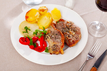 Appetizing pieces of roasted lamb leg with side dish of baked potatoes and red pepper ..
