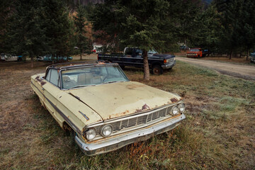 Rusty, vintage convertible car abandoned in a field, surrounded by other old vehicles. A forgotten...