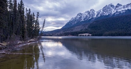 Fototapeta premium Serene mountain Yellowhead Lake at twilight. Snow-capped peaks reflect on the still water. Peaceful landscape. Jasper National Park, British Columbia, Canada