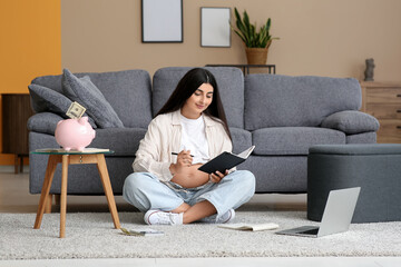 Fototapeta premium Young pregnant woman with notebook sitting on floor at home. Maternal Benefit concept