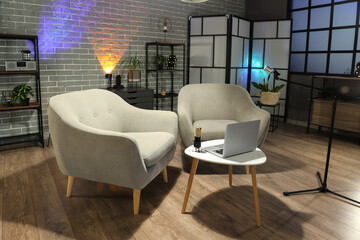 Interior of dark studio with podcaster's workplace, shelf units and glowing lamps