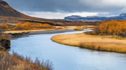 Obraz premium A serene river meanders through an autumnal landscape beneath a cloudy sky