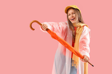 Cute teenage girl in raincoat with orange umbrella on pink background