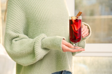 Young woman holding glass cup of hot mulled wine at home, closeup
