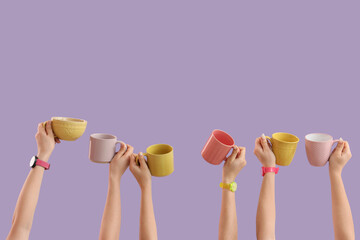 Female hands with different mugs on lilac background