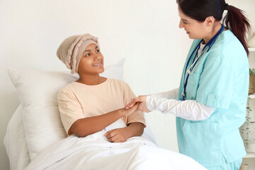 Obraz premium Teenage African-American girl after chemotherapy with doctor holding hands in hospital room
