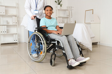 Teenage African-American girl using laptop in wheelchair with doctor at hospital