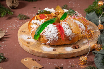 Colorful candied fruits and powdered sugar on a traditional Bolo Rei or Kings Cake, set on a wooden board amidst warm holiday decorations and lights. Is tradicional for Christmas in Portugal
